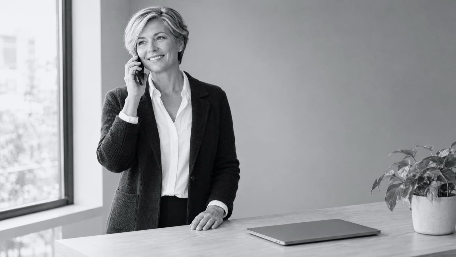 A business owner smiling on a phone call at her desk, a closed laptop in front of her.